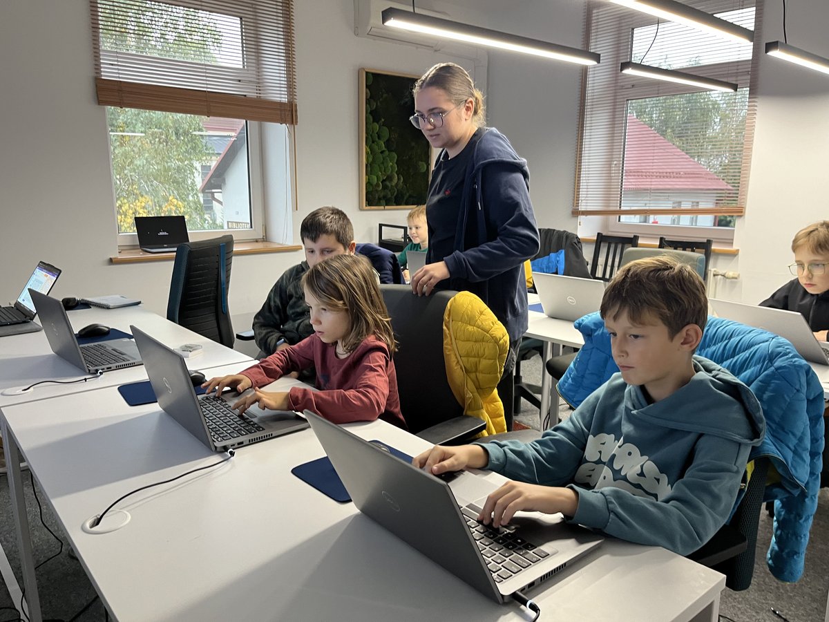 Instruktorka JuniorAI prowadzi zajęcia — grupa dzieci przy laptopach